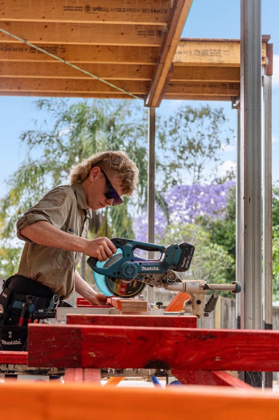 Cutting timber outside, with jacaranda in the background